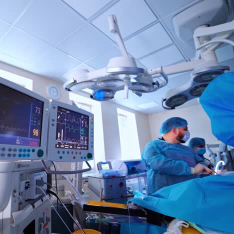 modern operating room indoors. two monitors showing heart beat and pulse. surgeons perform operation and use medical equipment in clinic.