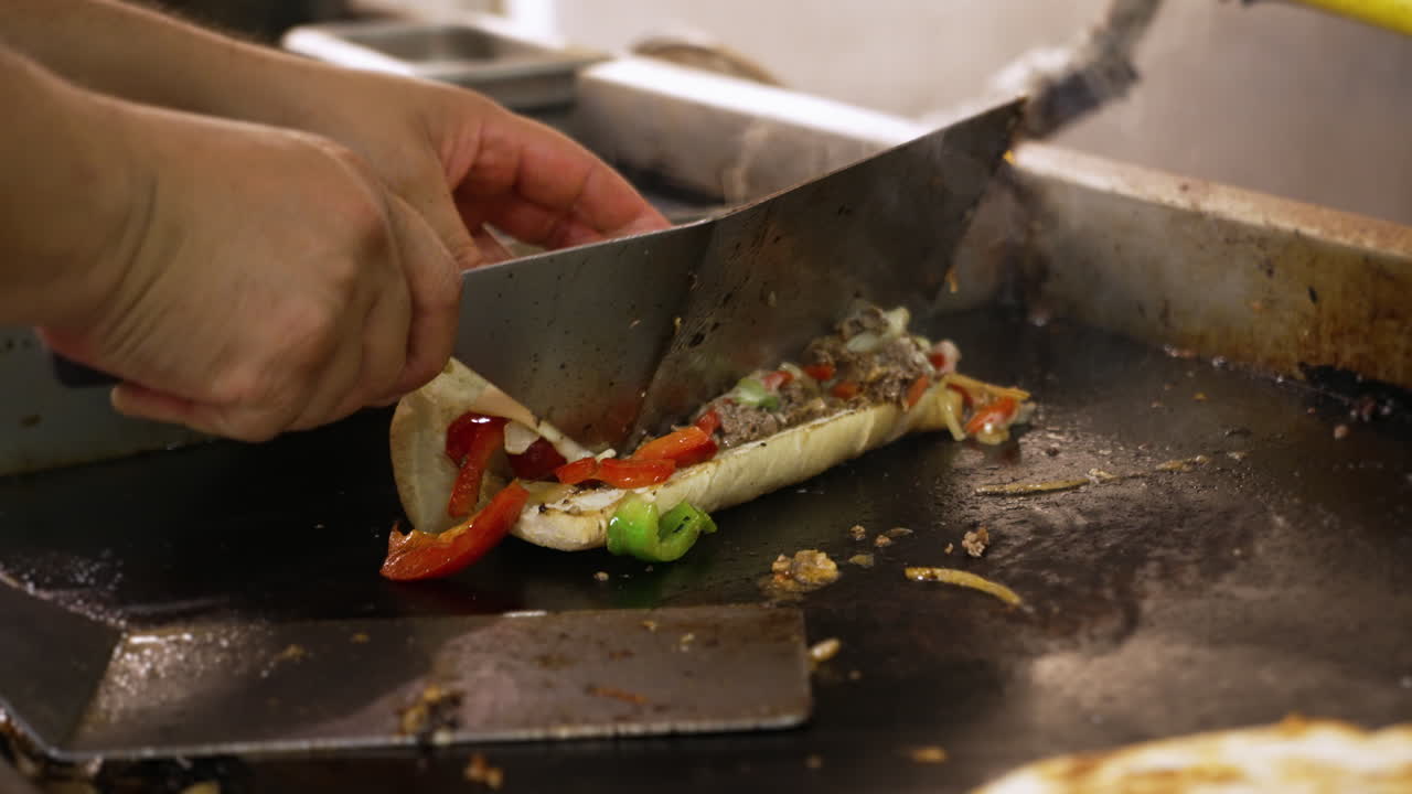 Cook uses spatula to stuff philly cheesesteak filling into steamed bun on flattop grill, close up slow motion 4K