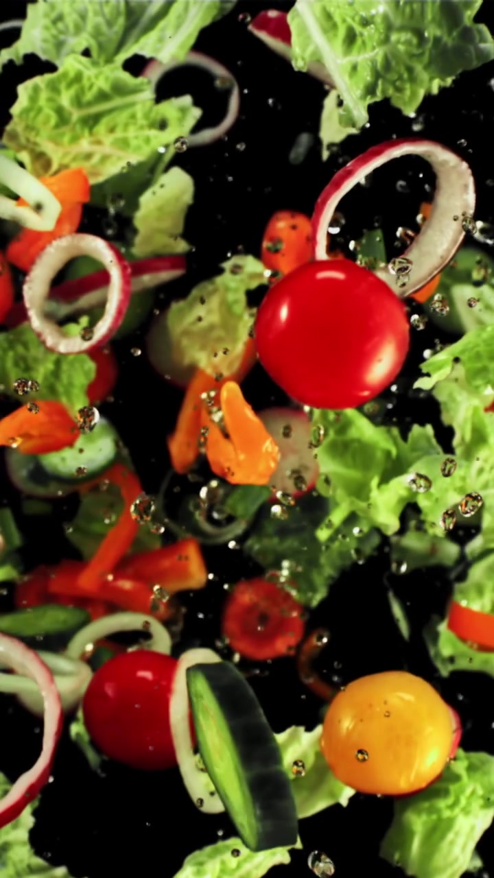 Verdure fresche per insalata che cadono al rallentatore con goccioline d'acqua