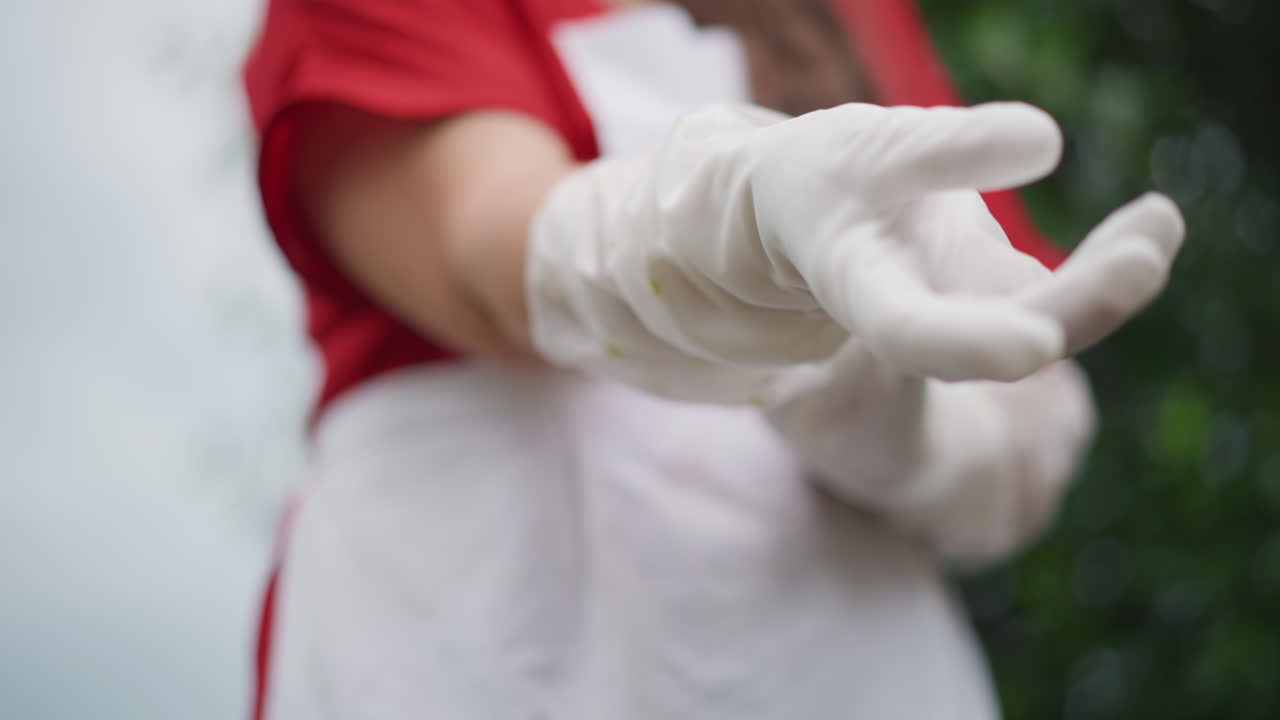 Mezza figura di rievocatrice storica bianca che indossa delicati guanti protettivi sopra il grembiule, con tessuto texturizzato e lavoro manuale accurato visibili, un movimento lento e metodico che suggerisce artigianato tradizionale e cura archivistica.