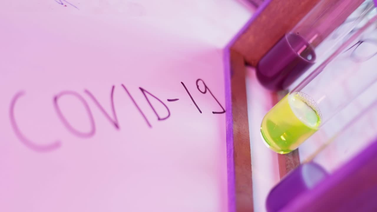 Laboratory desk with glass tubes containing colorful liquid solution and Covid-19 word written nearby