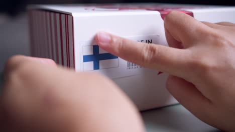 Hands-applying-MADE-IN-FINLAND-flag-label-on-a-shipping-cardboard-box-with-products