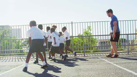 teacher plays football with young kids in school playground