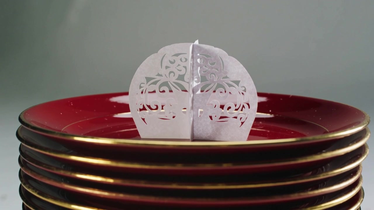 Pulling back camera revealing laser-cut ornament on stacked red plates on table, showing gold rims