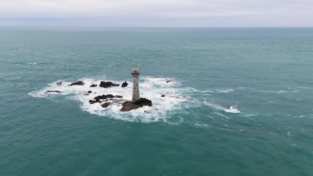 vuelo hacia el faro de hanoi guernsey hacia el mar en un día nublado brillante con rocas y salpicaduras marinas y olas espumosas