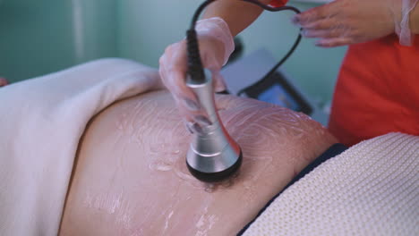 woman does vibromassage to plump client in clinic closeup