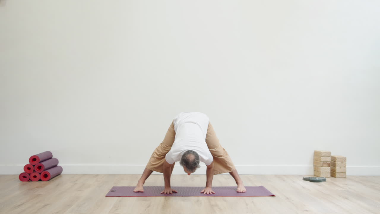 Uomo che esegue la posa yoga del piegamento in avanti a gambe divaricate in studio