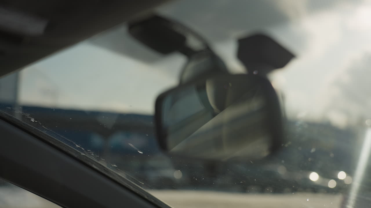 close up rearview mirror inside vehicle with soft focus effect capturing bright bokeh lights and blurred parked cars outside with warm sunlight reflecting on windshield on clear day