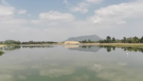 beautiful scenic lake with a clear mirrored reflection of a bird flying across in phetchaburi, thailand