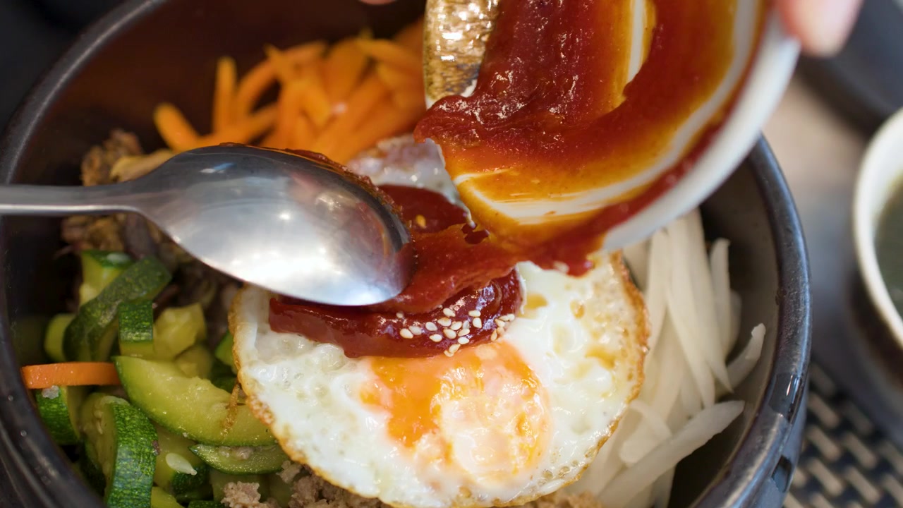 Pengambilan gambar jarak dekat pasta cabai merah yang dituang ke atas mangkuk batu bibimbap