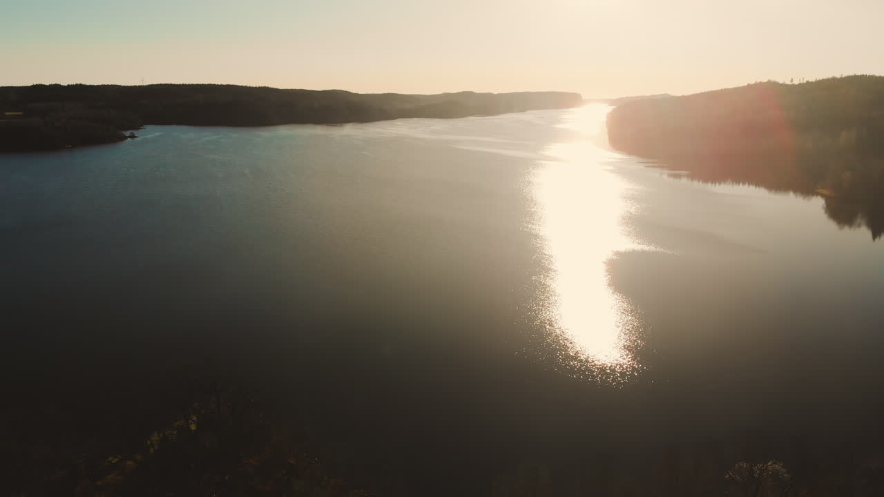 Jasné sluneční světlo odrážející se ve vodě jezera, letecký pohled na přírodní krajinu.