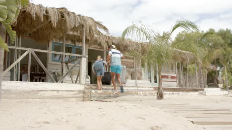 familia caucásica feliz caminando con equipaje en la casa de la playa