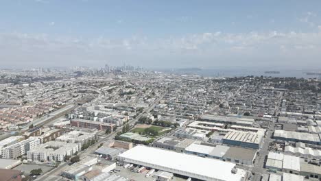 this drone shot offers a sunny, scenic vista of san francisco's bayview neighborhood, commercial and residential areas, downtown skyline, and yerba buena island, all bustling with bay activity