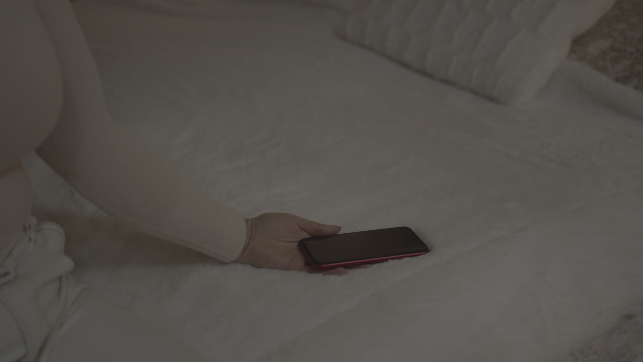 침대에 앉아 실망한 소녀가 손바닥에 들고 있는 아이폰을 침대 담요에 갑자기 떨어뜨립니다.