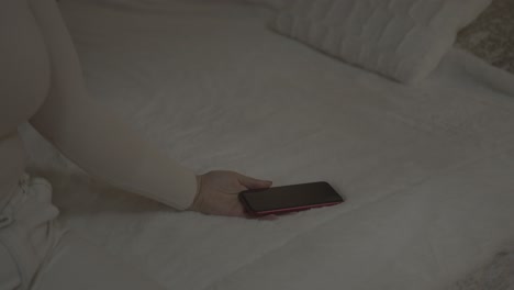 a disappointed girl sitting on the bed abruptly drops the iphone she is holding in her palm on the blanket of the bed