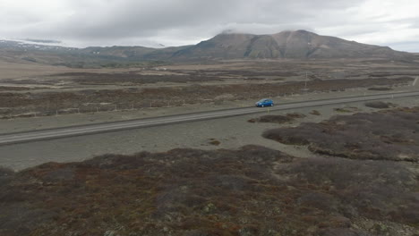 aerial view with tracking at medium distance to blue car and over the road leading to the icelandic rock formation of hvitserkur on a dull day