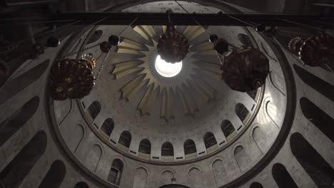 Slow-pull-back-shot-of-high-domed-ancient-church-ceiling,-revealing-beautiful-hanging-lights,-as-bird-flys-out-of-spire