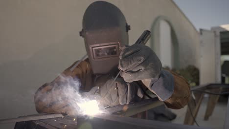 person with protection mask is welding a metal object, sparks shooting