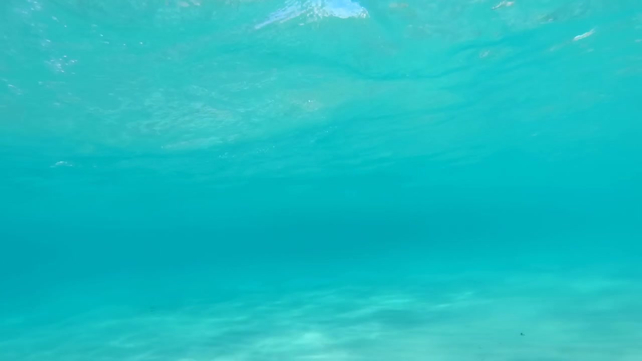 Agua turquesa vacía vista desde abajo con suaves ondulaciones en la superficie, tonos tropicales claros y luz natural suave, creando un fondo acuático abstracto y tranquilo.