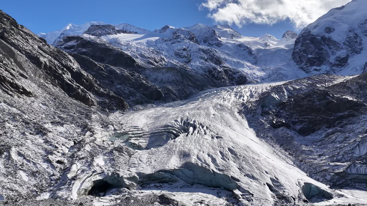 An aerial, high-altitude view of a large, crevassed glacier in the Swiss Alps a. The snow and ice are surrounded by dark, rugged peaks