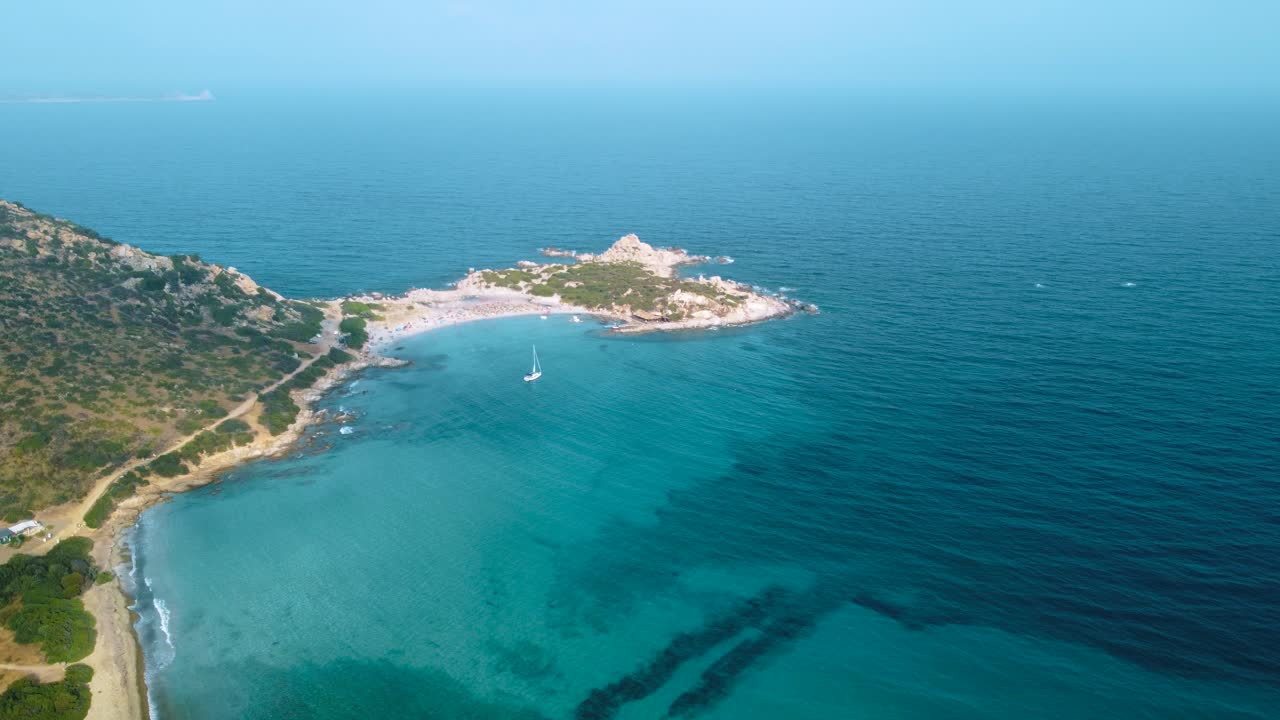 Clear blue turquoise and calm water at a natural sand beach coast bay in Sardinia, Italy with sun and sailing ship