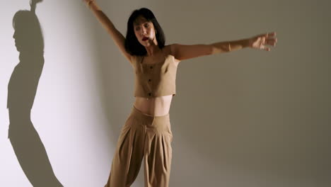noticing elongated shadow, asian female dancer tracing outline in spotlight on white wall
