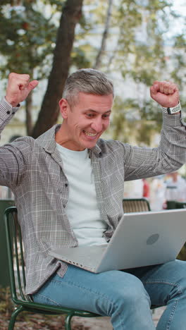 happy man freelancer working on laptop screams in triumph win celebrating success sitting on chair