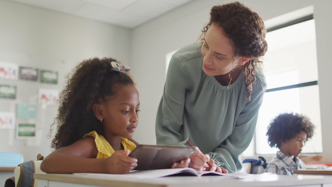 video de una feliz maestra caucásica explicando la lección a una niña afroamericana que sostiene una tableta