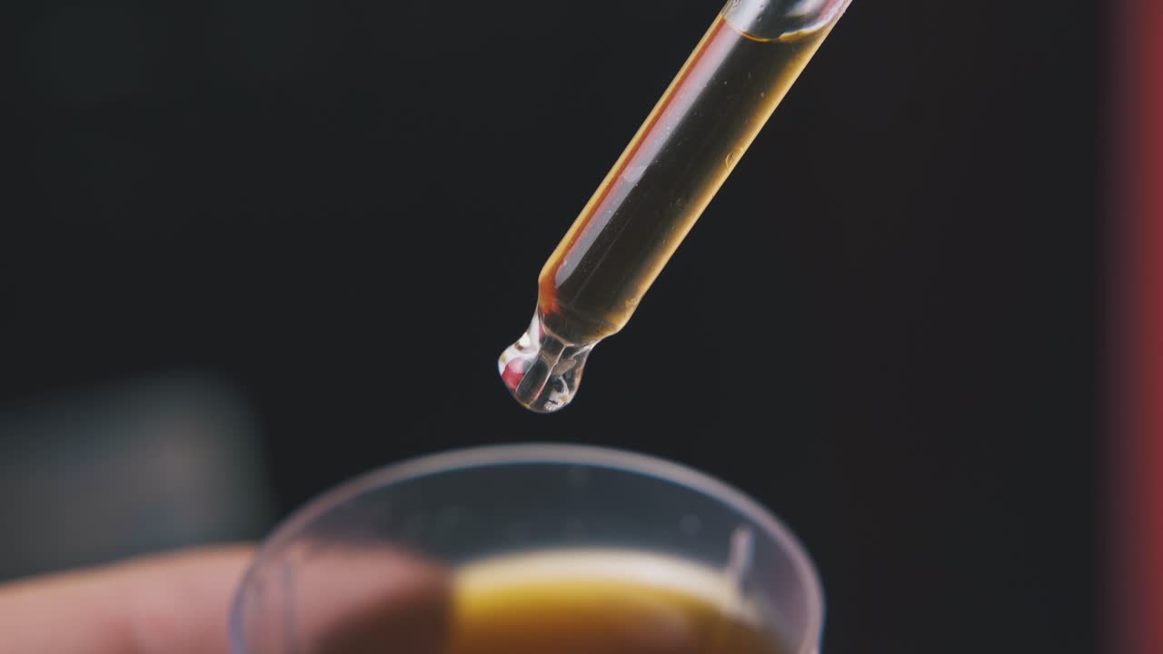 el hombre toma líquido con pipeta del vidrio sobre un fondo oscuro