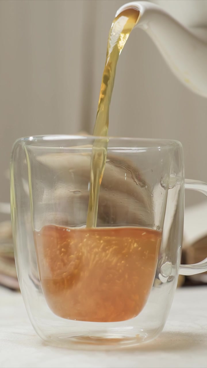 Primo piano di una tazza di vetro a doppia parete trasparente mentre viene versato il tè. La condensa si forma sullo strato interno mentre le bolle salgono. La scena rimane focalizzata esclusivamente sull'azione di versare per tutta la durata.