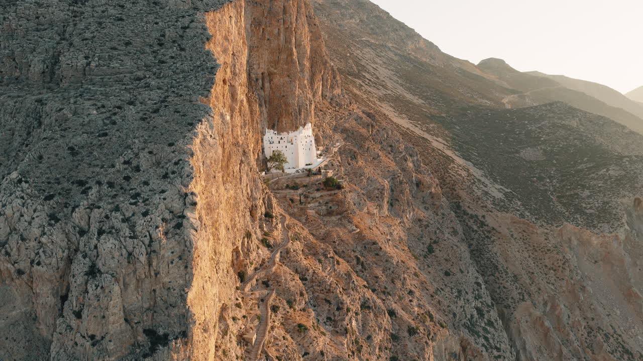 Drone reveals Panagia Hozoviotissa Monastery at Sunrise on Amorgos Island Illuminated by Golden Cliffside Light Greece