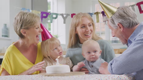 grandparents with mother singing happy birthday to grandson at first birthday party at home