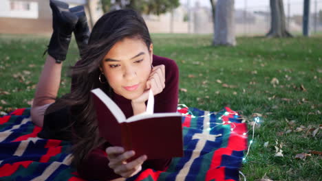 una estudiante hispana leyendo y estudiando un libro de texto escolar en un campus universitario al atardecer