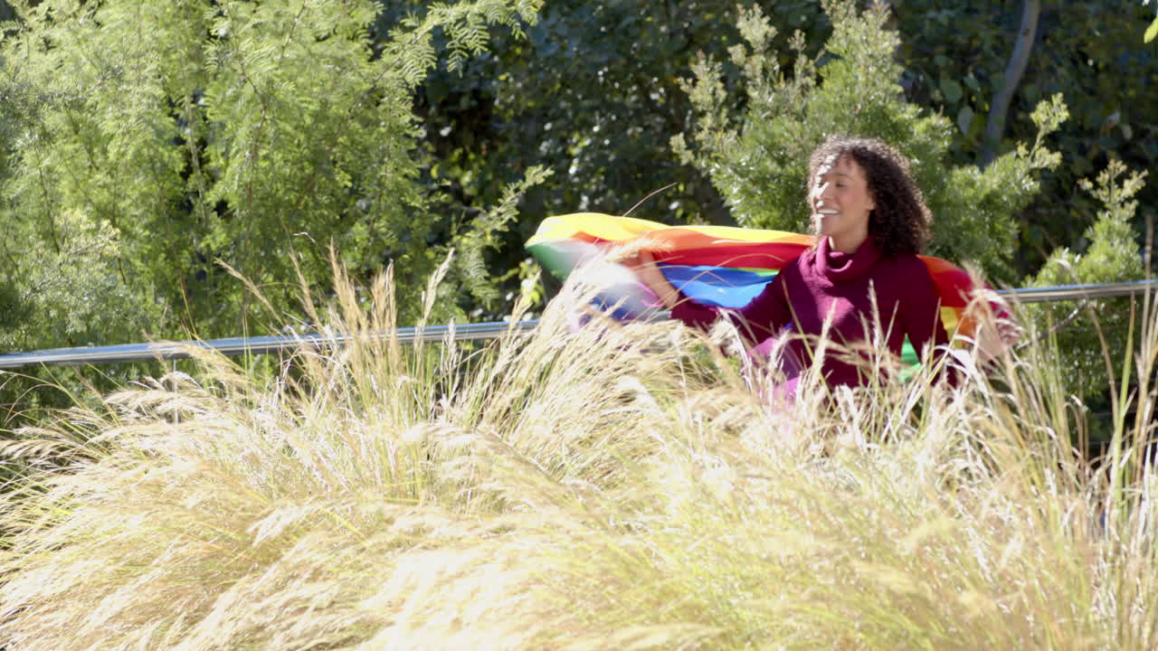 Woman running with rainbow flag in nature, celebrating LGBTQ+ pride outdoors