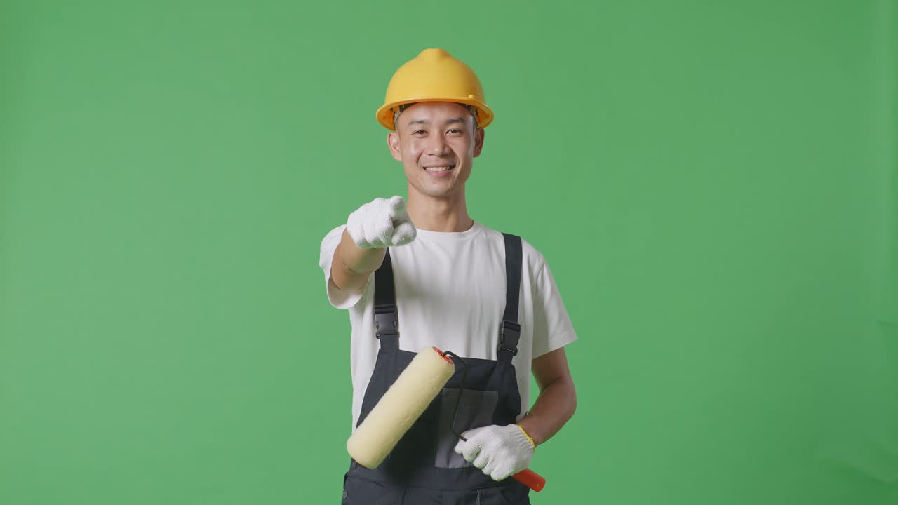 Asian Man Painter Wearing Safety Helmet Smiling And Touching His Chest Then Pointing At You While Standing In The Green Screen Background Studio