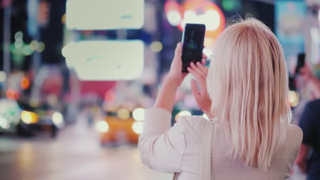 tourist takes pictures with a smartphone on the famous times square in new york rear view