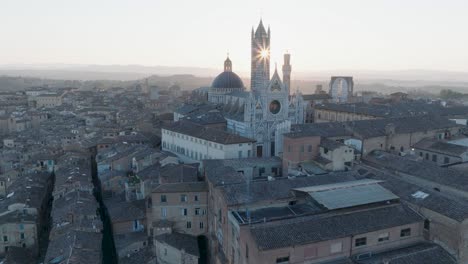 aerial view of siena, tuscany, italy at sunrise with torre del mangia and sun flare through duomo di siena, in 4k