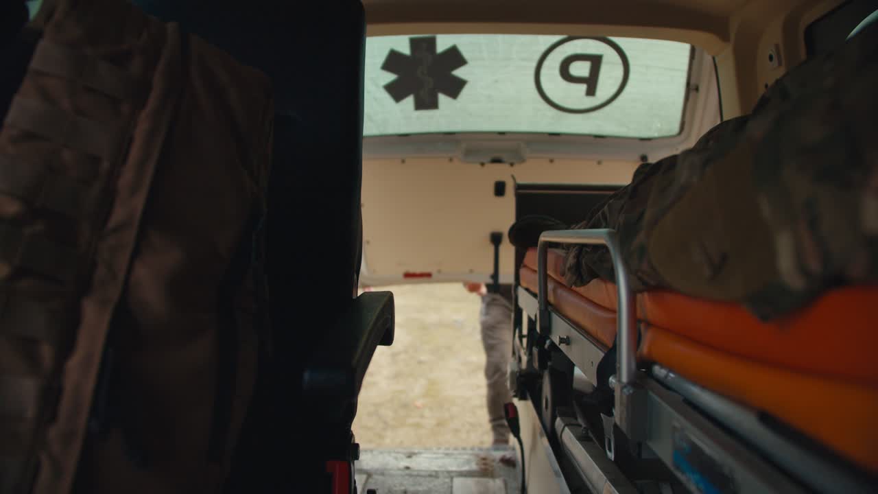 vista desde el interior de una ambulancia un hombre en un uniforme de camuflaje yace en un portador en la cabina de la ambulancia y las puertas traseras del coche están cerradas mientras proporciona asistencia médica en una zona de combate