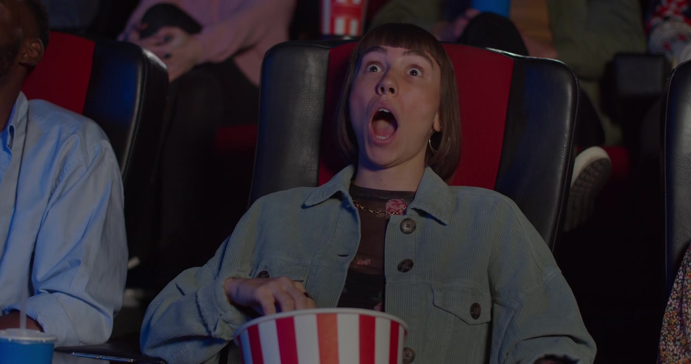 Ung kvinde reagerer chokeret, mens hun ser en film i en biograf