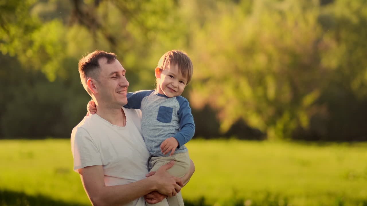 Mani di papà che tengono il figlio piccolo, felice, sorridente e carino, mentre giocano insieme nella natura in campagna. Ripresa POV di una famiglia spensierata che si gode il weekend, rilassandosi e divertendosi all'aperto, con inquadratura dall'alto.