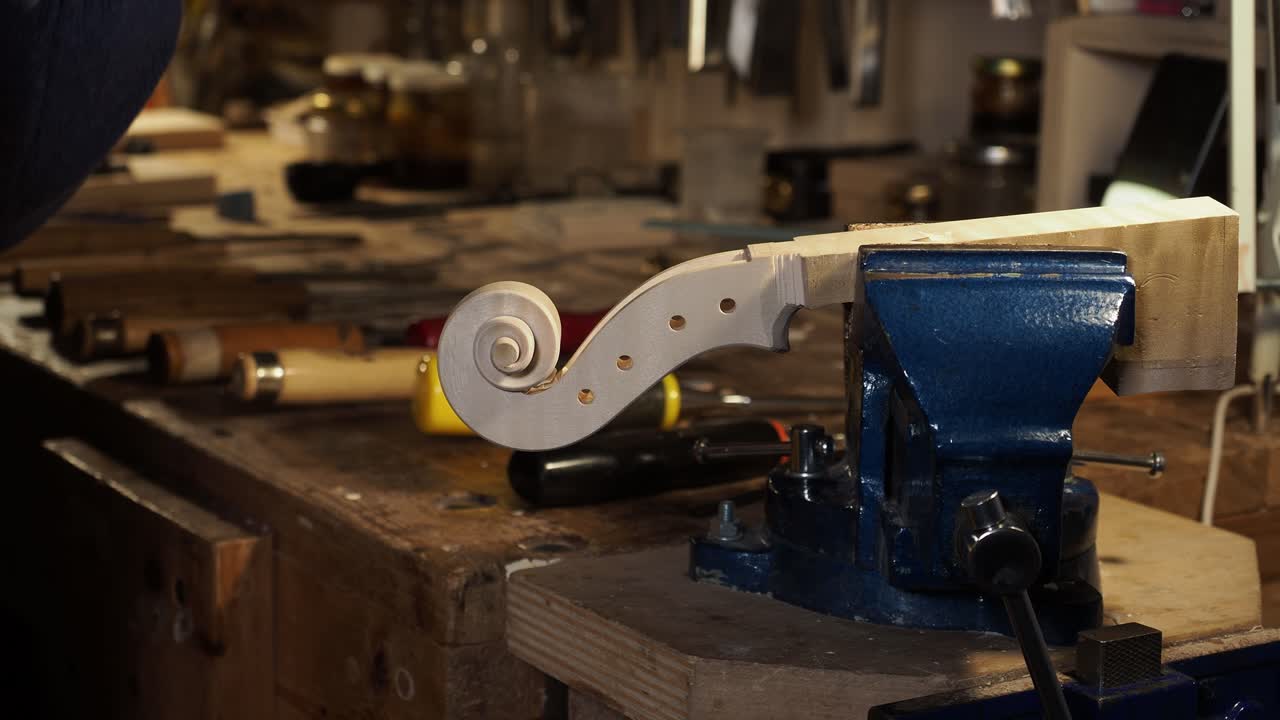Violin scroll under construction clamped in woodworking vise, artisan craft process and traditional luthier workshop atmosphere