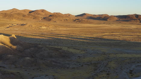 backwards aerial view of the textured landscape around the trona pinnacles during a bright yellow sunrise