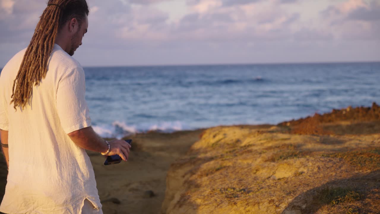 Man using smartphone by the ocean at sunset
