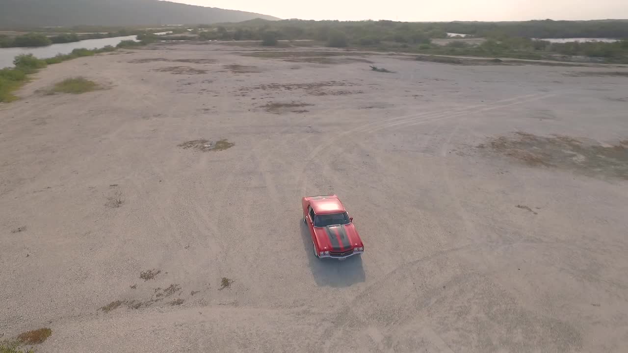vista aérea de un viejo coche muscular americano en un desierto durante una puesta de sol junto a un río