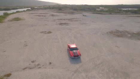 vista aérea de un viejo coche muscular americano en un desierto durante una puesta de sol junto a un río