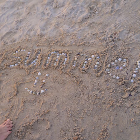 boy is putting with pebbles the word summer on a sand beach. child laying the smiley sign with small shells on sand background. happy childhood.