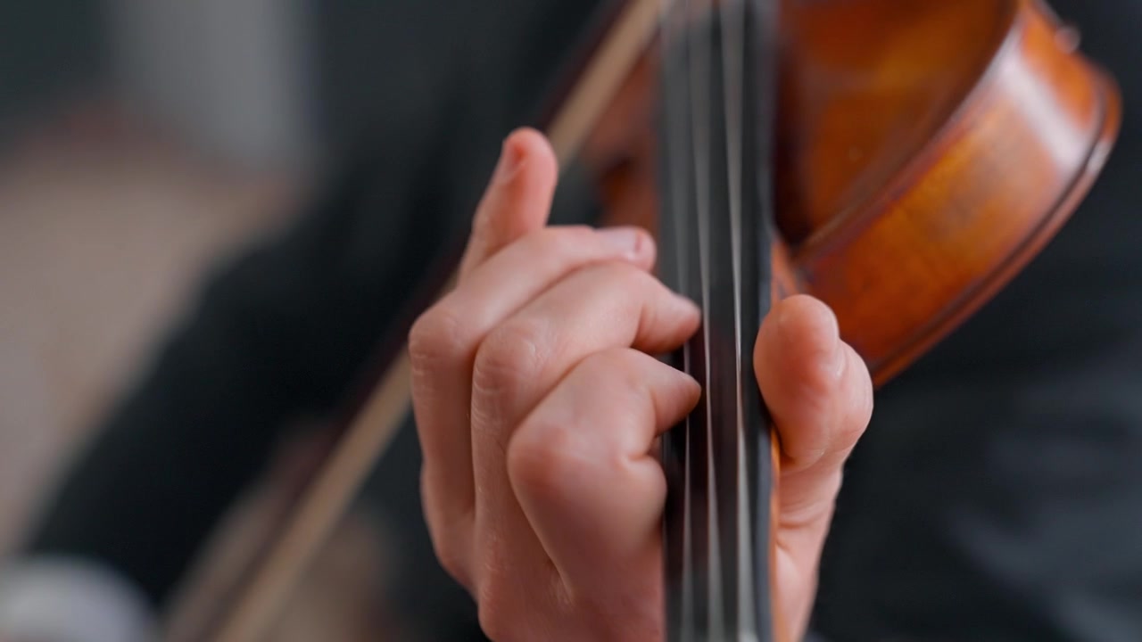 Primo piano della mano di un musicista che suona le corde del violino