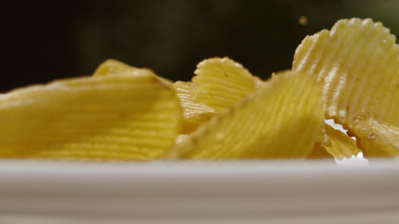 Macro Close Up of Potato Chips Crisps Tumbling on China Plate Outdoors - 4K Food Clip
