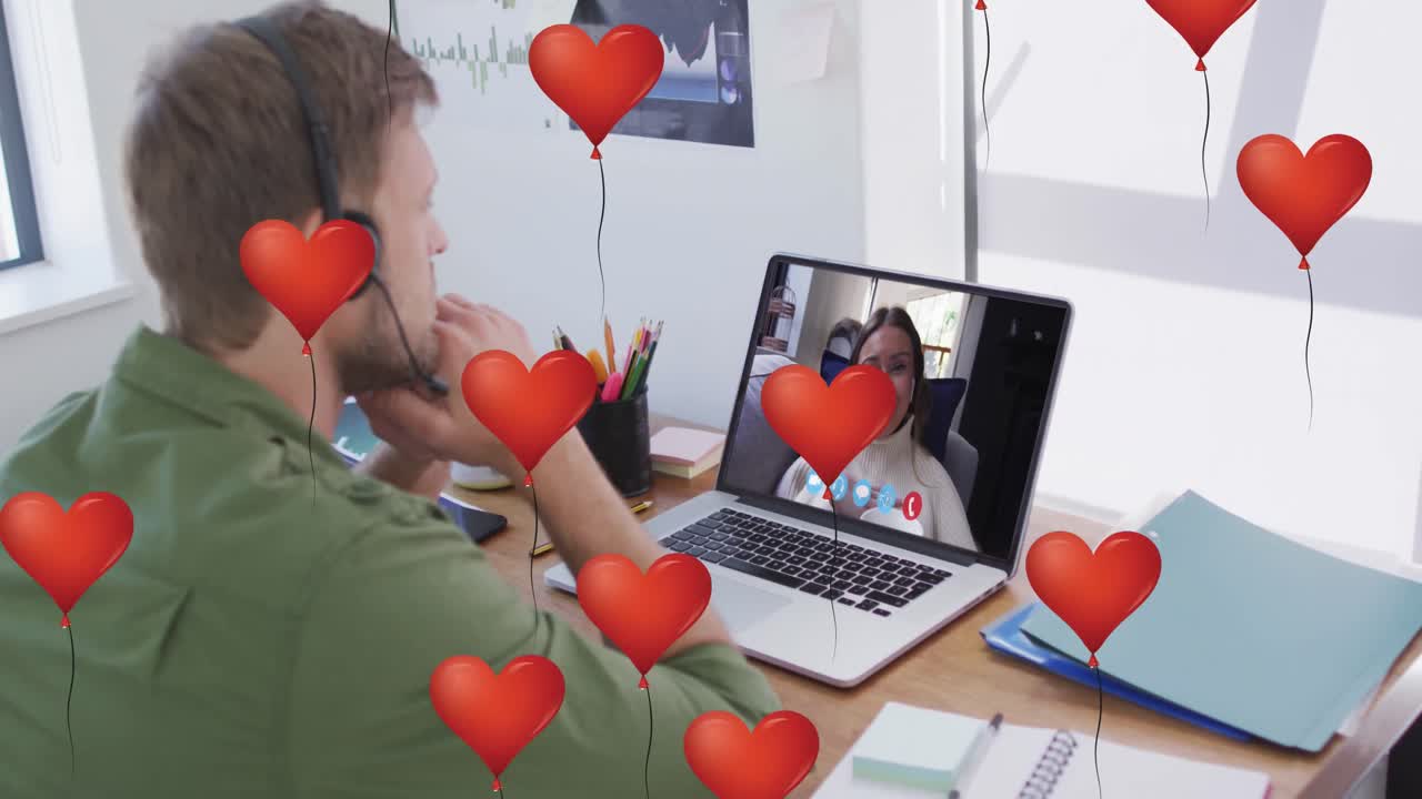 Múltiplos balões de coração flutuando e homem de headset em videochamada no laptop no escritório ao fundo.
