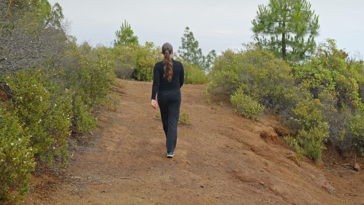 mujer caminando en la naturaleza verde de tenerife, turista en trajes negros